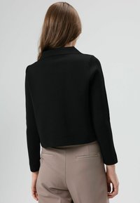 Zwarte cropped jas met lange mouwen en een reverskraag, gemaakt van een gestructureerde stof. Gecombineerd met lichtbeige hoge taillebroek.