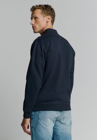 Navyblauwe sweatshirt met opstaande kraag, gemaakt van zachte stof. Kenmerkt zich door ribgebreide manchetten en zoom. Draagt bij lichte spijkerbroek.