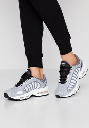 Des baskets de sport grises présentent une tige texturée avec des accents blancs, des lacets noirs et une unité d'air visible dans la semelle.