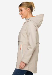 Lätt beige regnjacka med huva, med en dragkedjeförsedd framficka med orange drag, elastisk midja och ett slätt, vattentåligt material.