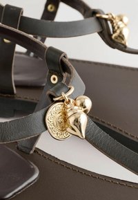 Gros plan sur des lanières de sandales en cuir marron foncé avec des breloques décoratives dorées attachées à une boucle.