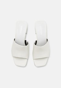 White open-toe slide sandals with a smooth faux leather upper, flat sole, and a wide cross-band design. Minimalist and modern style.