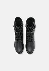 Bottes noires en cuir au niveau de la cheville avec une texture lisse, un laçage à l'avant et des zippers sur le côté pour un enfilage facile. Design à bout rond et semelle plate.