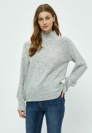 Hellgrauer Pullover mit hohem Kragen, gerippten Bündchen und Saum. Weiche Textur und entspannte Passform, kombiniert mit dunkelblauen Jeans.