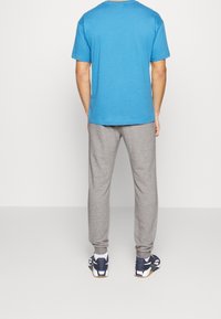 Blå kortärmad t-shirt, grå mjukisbyxor och marinblå träningsskor. Materialet verkar mjukt; byxorna har elastiska muddar och en avslappnad passform.