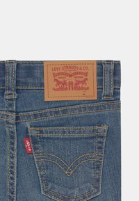 Vaqueros de denim azul de Levi's con un parche de cuero marrón con impresión roja, costuras doradas y una pequeña etiqueta roja en el bolsillo trasero.