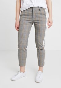 Pantalon à carreaux gris et jaunes avec une coupe ajustée, doté d'une bande latérale, d'ourlets retroussés et d'une texture de tissu lisse. Assorti à des baskets blanches.