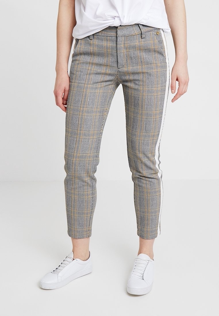 Pantalon à carreaux gris et jaunes avec une coupe ajustée, doté d'une bande latérale, d'ourlets retroussés et d'une texture de tissu lisse. Assorti à des baskets blanches.