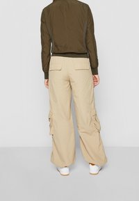 Olivově zelená bomber bunda s žebrovanými manžetami a límcem, spárovaná s béžovými cargo kalhotami s několika kapsami a volným střihem.