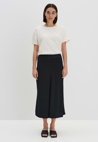 Wit gestreept kortmouwtopje gecombineerd met een zwarte enkellange rok. Glad textuur; minimalistisch ontwerp met een relaxte pasvorm. Zwarte instappers.