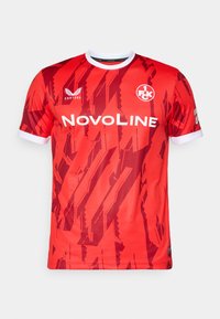 Maglia rossa a maniche corte con un motivo geometrico, dettagli bianchi nel colletto e nelle maniche, e loghi degli sponsor sul davanti.