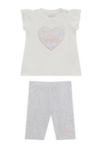 T-shirt bianco in cotone con maniche corte a sbuffo, con una grafica di cuori rosa e blu; leggings abbinati con stampa floreale leggera blu.