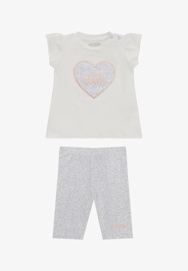 T-shirt bianco in cotone con maniche corte a sbuffo, con una grafica di cuori rosa e blu; leggings abbinati con stampa floreale leggera blu.