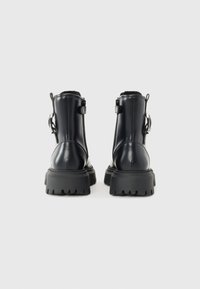 Botas de tobillo sintéticas negras con una suela de goma gruesa, cremalleras laterales y una lengüeta en la parte posterior para facilitar el calzado. Acabado liso y brillante con un minimalismo en los detalles.