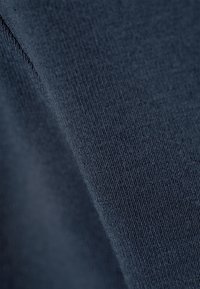 Σκούρο μπλε ύφασμα που δείχνει μια κοντινή λήψη μιας ομαλής, υφασμάτινης επιφάνειας με λεπτή ραβδώσεις, υποδεικνύοντας ένα απαλό και ελαστικό υλικό.