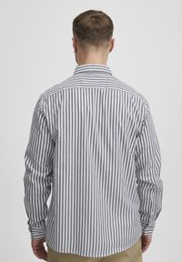 Camicia a maniche lunghe con colletto a bottoni, caratterizzata da strisce verticali grigie e bianche, realizzata in cotone leggero con una consistenza liscia.