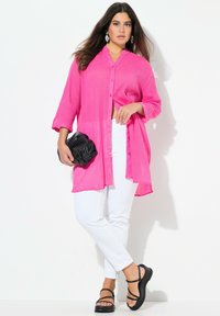 Fuchsia button-up shirt met driekwart mouwen, gecombineerd met witte skinny jeans en zwarte sandaaltjes met bandjes. Zwarte clutch is inbegrepen.