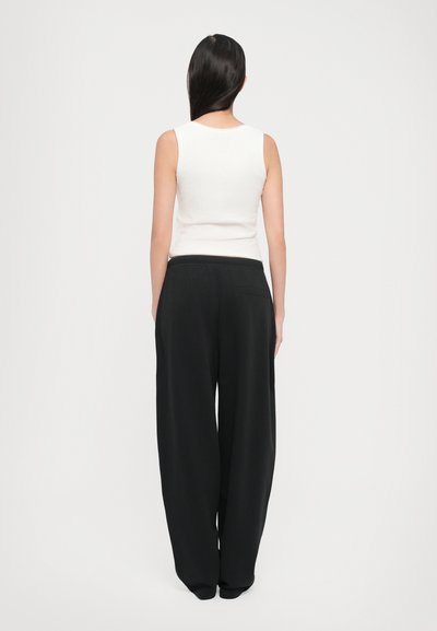 White ribbed tank top with black wide-leg pants. Pants feature an elastic waistband and a single back pocket. Smooth texture, relaxed fit.