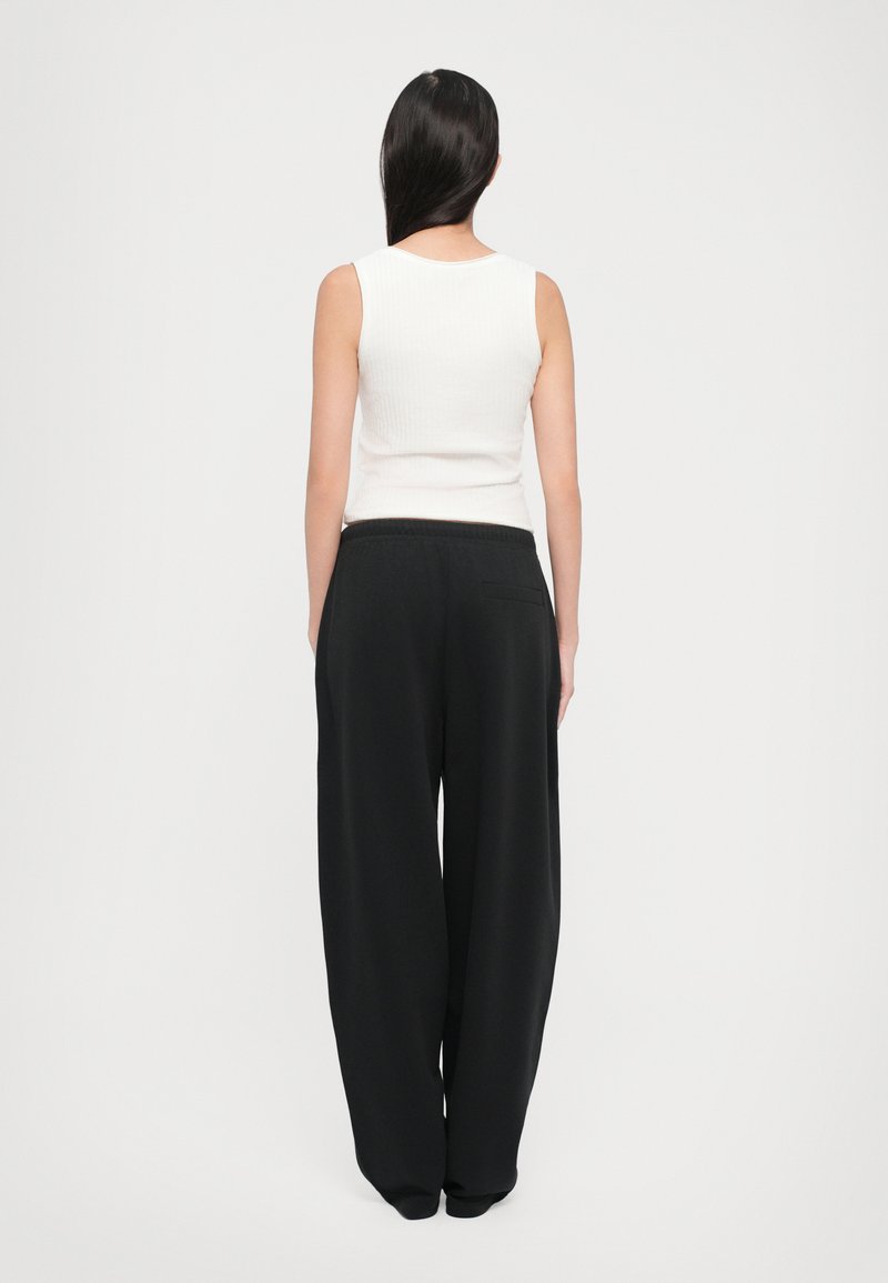 Débardeur blanc à côtes avec un pantalon large noir. Le pantalon présente une taille élastique et une poche arrière unique. Texture lisse, coupe décontractée.