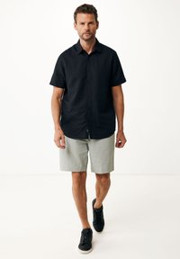 Svart kortärmad skjorta med knappar, ljusgrå shorts och svarta sneakers. Slät tygkvalitet, avslappnad passform och enkel design.