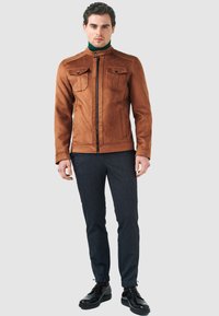 Brun faux suede jacka med ståkrage, framside dragkedja och två bröstfickor. Bärs med mörka texturerade byxor och svarta skor.