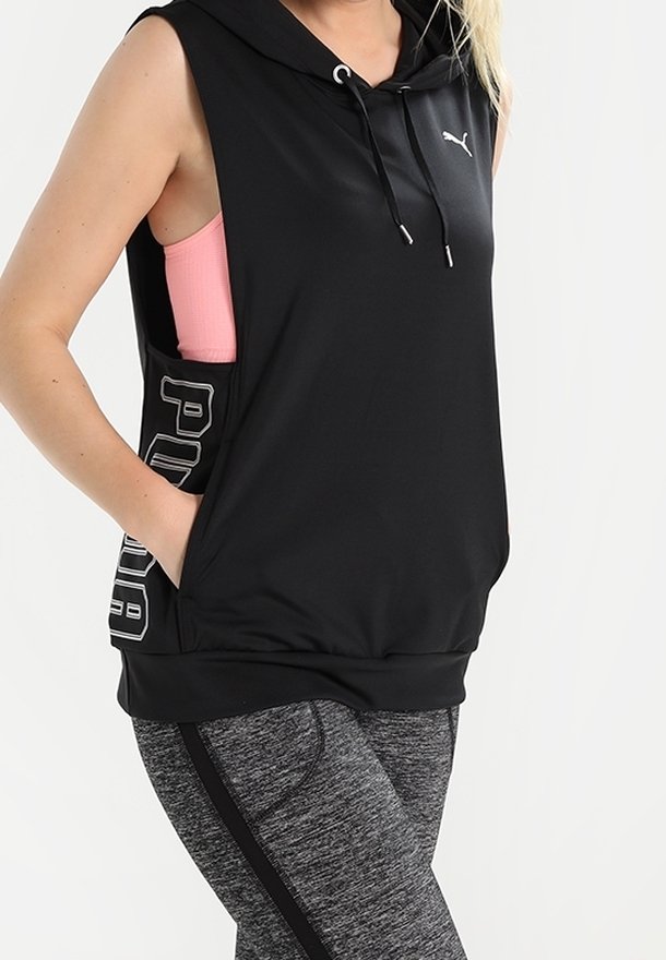 Personne portant un sweat à capuche Puma noir sans manches sur un débardeur rose et des leggings de sport gris avec bande noire, tenue sportive décontractée.