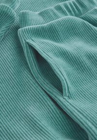 Türkisfarbenes geripptes Gewebe mit einer weichen Textur und ausgeprägten vertikalen Linien, teilweise gefaltet und mit sichtbarer Öffnung.