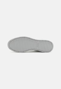 Hvit sneakersåle med en teksturert grå gummioverflate, som har horisontale spor og preget merkevarelogo "BOSS." Rund tådesign.