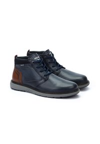 Botas de cuero navy para el tobillo con acentos marrones, punta redonda, suela de goma gris y cordones navy. Presenta un collar acolchado y detalle de logo.