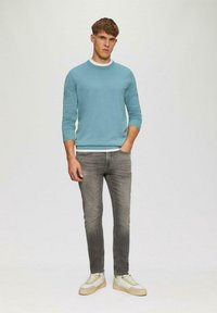 Hellblauer Pullover mit einem weißen Rundhalsausschnitt, kombiniert mit grauen Jeans und beigen Sneakers. Der Schnitt ist lässig, mit langen Ärmeln und einer glatten Textur.