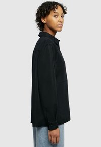 Zwarte lange mouwen shirt met een kraag, enkele borstzak en knopenmanchetten. Lichtgewicht stof met een gladde textuur, gedragen met lichtblauwe jeans.
