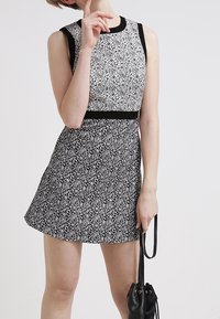 Svart och vit ärmlös klänning med blommönster, figurnära livstycke och utsvängd kjol. Har en enhetlig svart midjeband och rund halsringning.