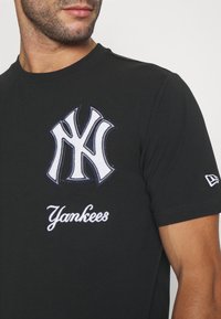 Czarny bawełniany t-shirt z dużym, białym haftowanym logo NY na piersi oraz napisem „Yankees” poniżej, również w białym hafcie. Krótkie rękawy.
