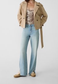 Béžový dvojitý trenčkot, top s hadím potiskem, světle modré široké džíny se bočními knoflíky a béžové tenisky s bílými tkaničkami.