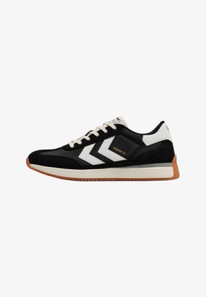Baskets de sport noires et blanches avec rayures chevrons blanches, lacets beiges, semelle en gomme et texte « Stadion 23 » sur le côté.