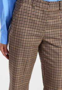 Persona che indossa pantaloni a quadri marroni e una camicia a maniche lunghe blu, con dettagli sulla texture e sul motivo del tessuto.