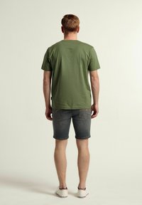 Camiseta de manga corta color verde oliva con cuello redondo, combinada con shorts de mezclilla. Los shorts son de un gris oscuro con bolsillos traseros y costuras visibles.