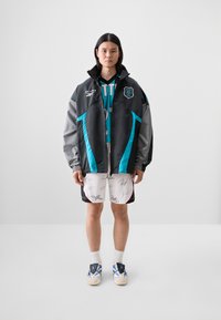 Fekete és szürke, oversized dzseki türkiz kiegészítőkkel, sportos kapucnis pulóver, fehér rövidnadrág fekete aláírásokkal, és kék tornacipő.