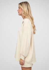 Lys beige oversized hettegenser med lange, puffede ermer og rund hals. Glatt tekstur og avslappet passform, som ender ved hoftene.