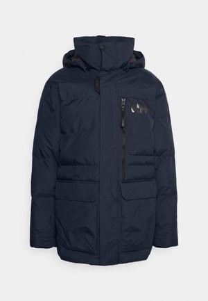 Chaqueta acolchada azul marino con un bolsillo con cremallera en el pecho izquierdo, dos bolsillos frontales con solapa y una capucha. Presenta herrajes y detalles de logo en color negro.