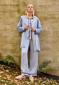 Light blue robe with a textured hood, paired with patterned light blue pants and a striped shirt. Beige slip-on shoes complete the outfit.