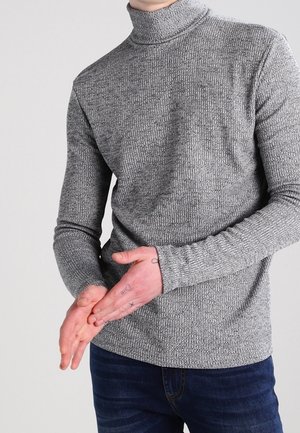 Pull en maille côtelée gris, à col roulé, avec des manches longues, en tissu texturé et au design ajusté. Associé à un jean bleu foncé.
