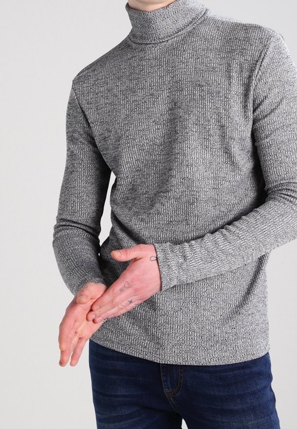 Grauer gerippter Rollkragenpullover mit langen Ärmeln, strukturiertem Stoff und tailliertem Schnitt. Getragen mit dunkelblauen Jeans.