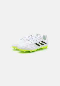 Botas de fútbol con una parte superior sintética blanca, que presenta rayas negras y un patrón texturizado; suela vibrante verde con tacos.