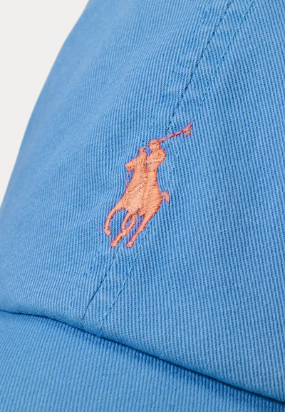 Light blue cap made of textured fabric, featuring an orange embroidered polo player logo on the front. Curved brim, six-panel design.