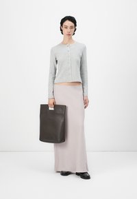 Grå strikket cardigan med lange ermer, tettsittende design, kombinert med en lys rosa maxiskjørt. Modellen holder en mørkebrun skinn tote bag.