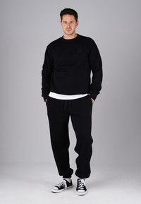 Black sweatshirt and joggers made of soft fabric, featuring a round neck, ribbed cuffs, and drawstring waistband, paired with black sneakers.