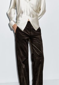 Kremowa satynowa bluzka z guzikami w zestawie z szerokimi spodniami z brązowego kordurowego materiału; gładka tekstura z pionowym żebrowaniem.