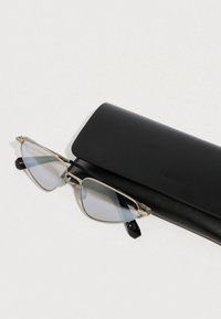 Óculos de sol com armação metálica e lentes azul claro, acompanhados de uma elegante caixa de couro preta. Os óculos apresentam um formato de olho de gato.