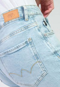 Lichtblauwe denim jeans met een hoge taille, voorzien van gele stiksels, een leren label aan de achterkant en een zakdetail met een gebogen ontwerp.